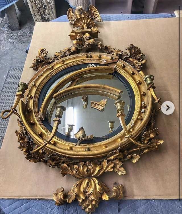 Damaged antique gilt oval mirror with broken glass and ornate carvings.