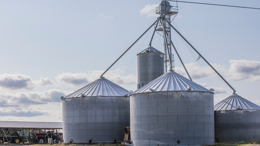 A row of metal silos sitting next to each other on a farm.