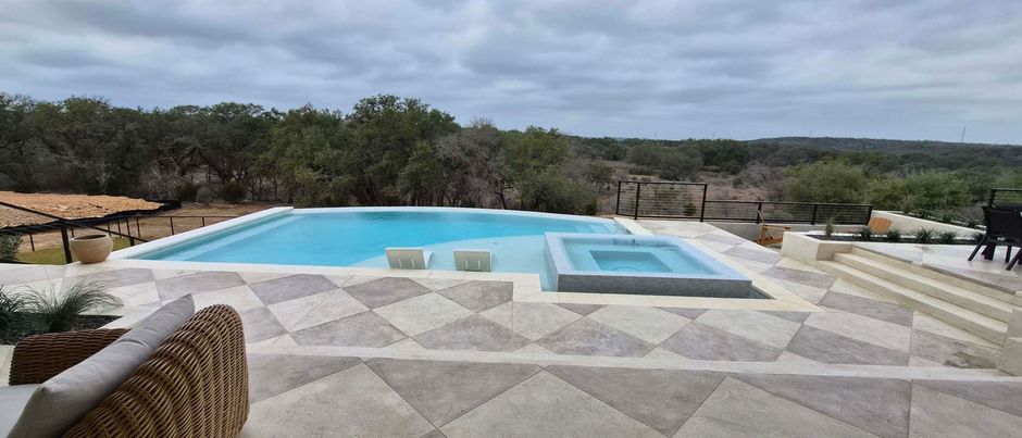 Swimming pool with spa and geometric patio overlooking a wooded landscape. Overcast sky.