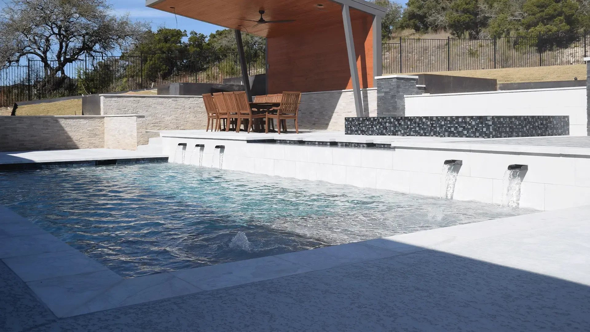 Poolside dining area with a modern wood and metal structure, overlooking a pool.