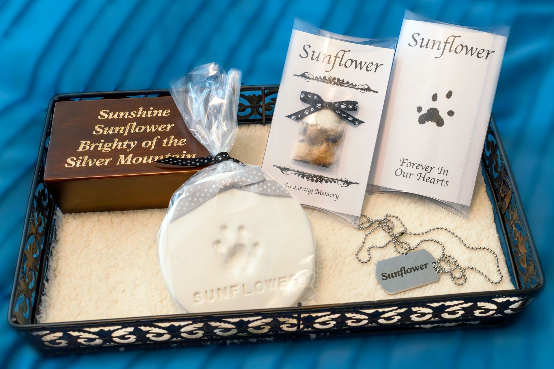 Pet memorial kit with a paw print, urn, sunflower pendant, and jewelry, on a tray.