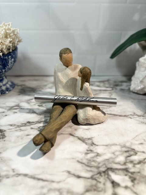A black pen gift set with a ribbon sits on books, in front of decorative objects.