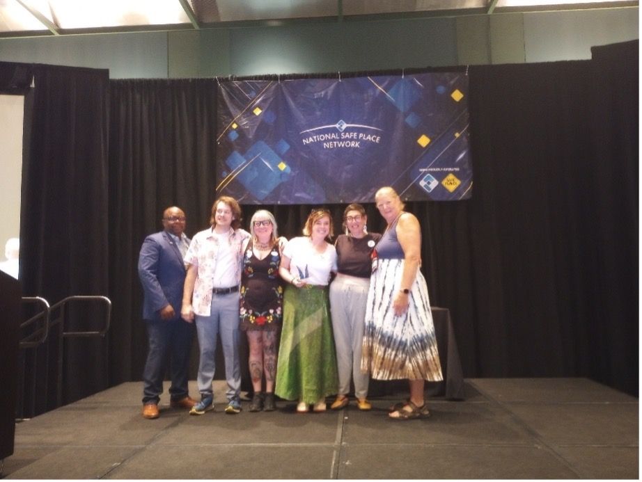 People on stage, banner in background; a group holding an award. Black curtain.