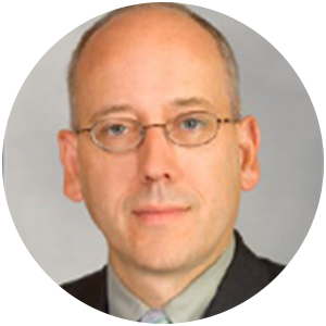 Man with glasses, light skin, close-up shot. He is wearing a suit jacket and collared shirt.