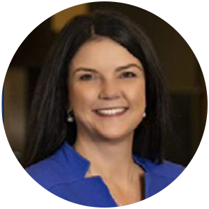 Woman with dark hair smiles, wearing a blue top, inside a building.
