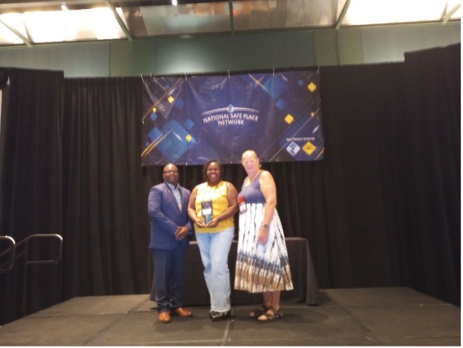 Three people on stage, holding an award in front of a banner.