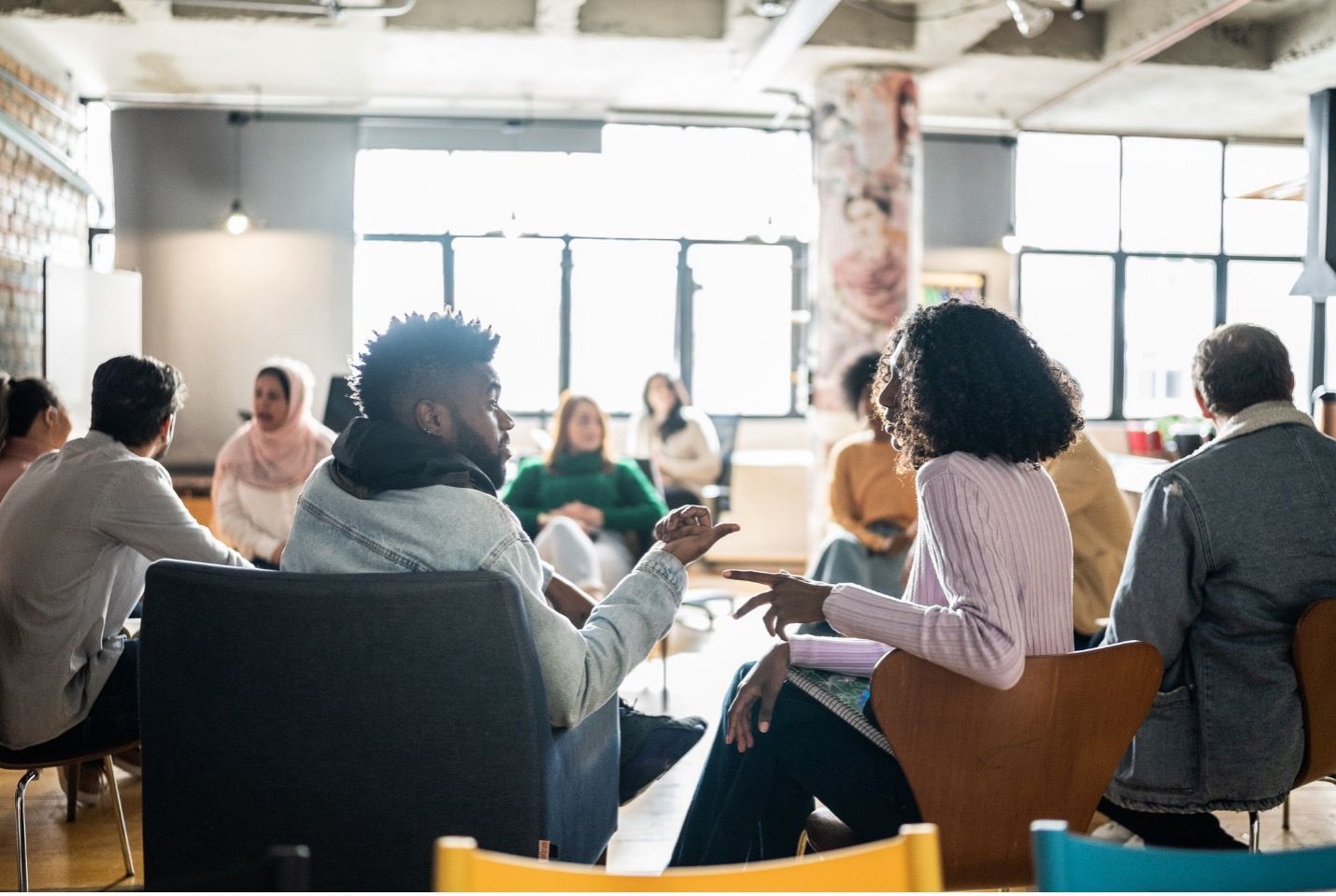 People in a circle, engaged in conversation within a bright, open-plan office setting.