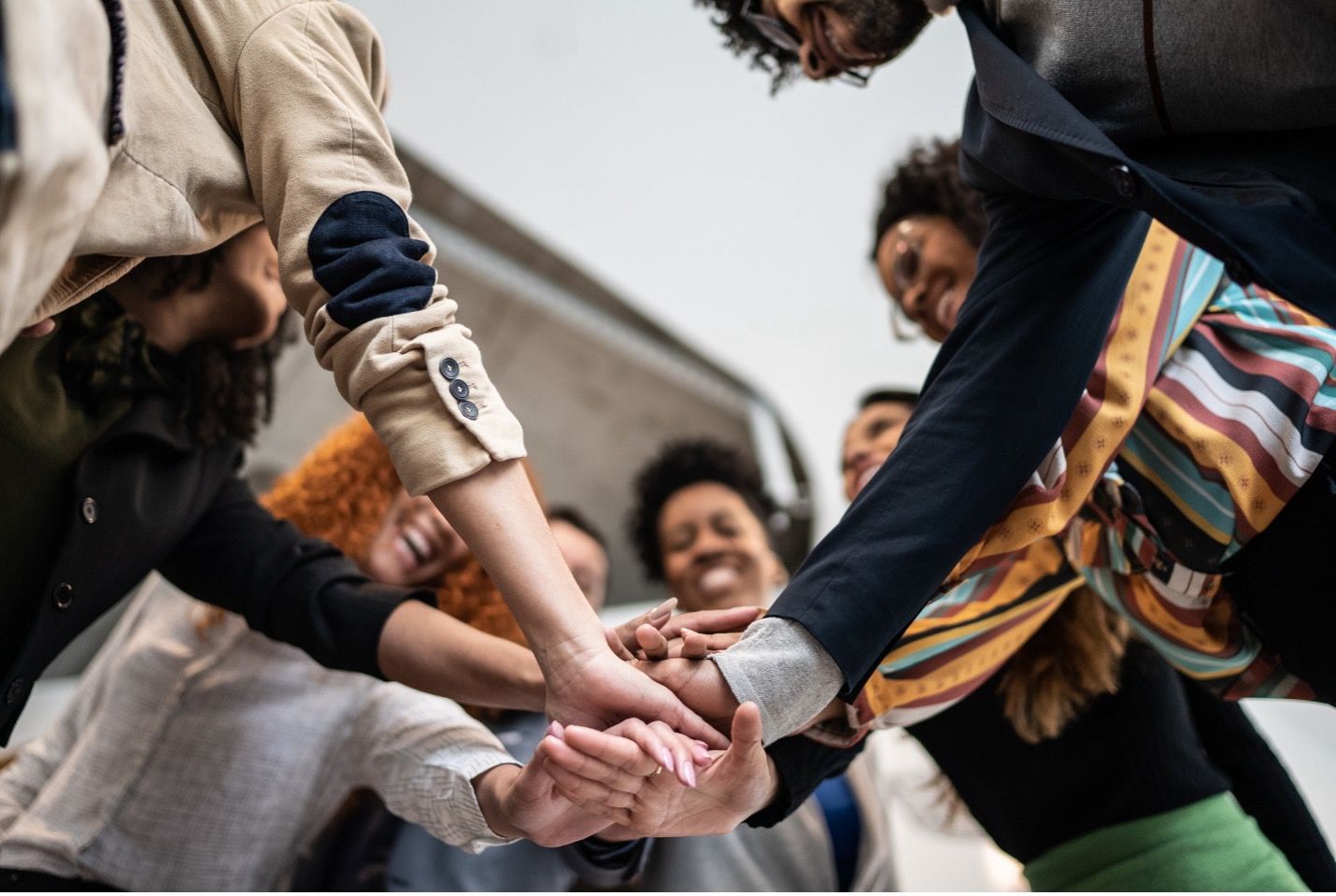 Hands of diverse people in a team huddle, smiling, arms together.