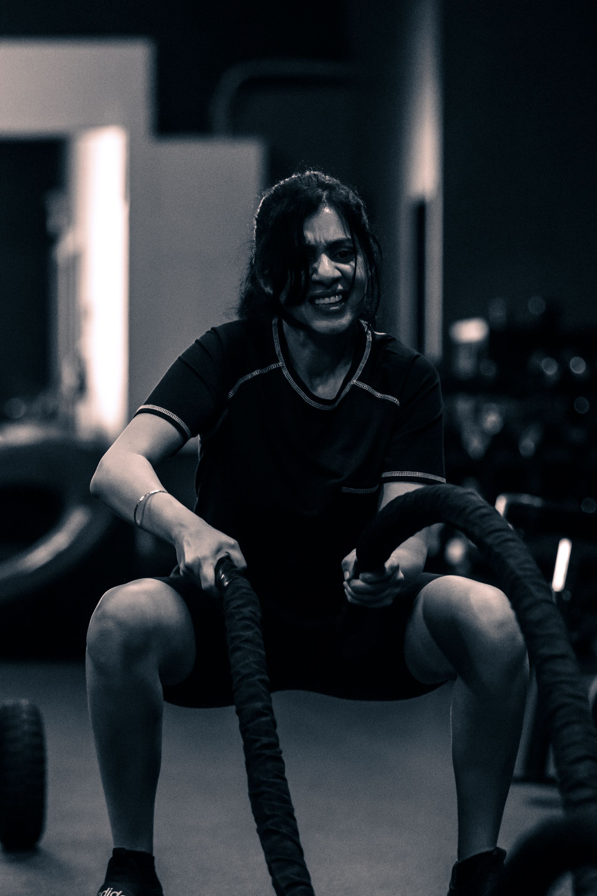 a woman is squatting down with a rope in a gym .