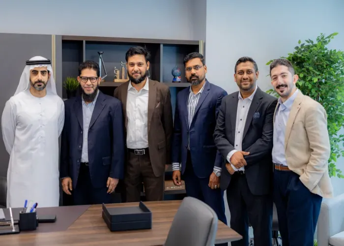 Six men in suits standing in an office; some smiling, possibly after a business deal.