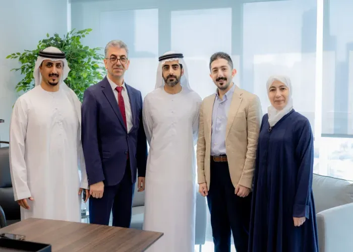 Five people in an office setting, two in traditional Arab attire, posing for a photo.