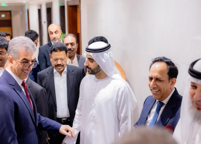 Men in suits and traditional Arab attire greet each other inside a building.