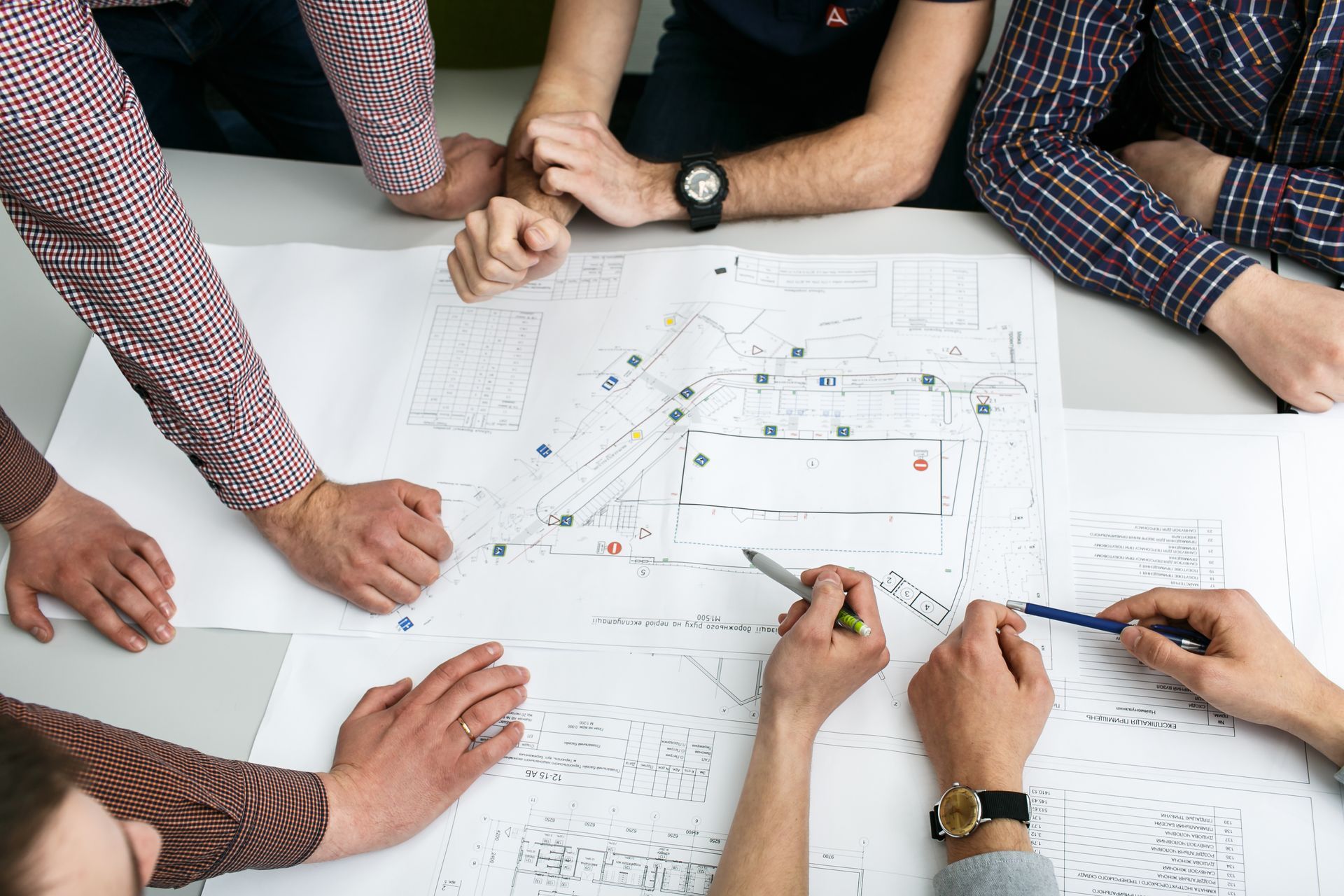People at a table reviewing blueprints, gesturing with pens, discussing a plan.