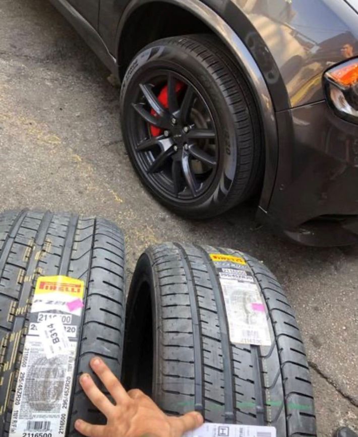 A person is holding a pair of tires in front of a car