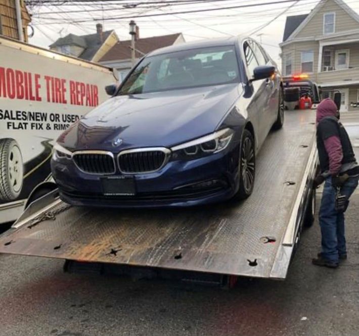 A blue car is being towed by a mobile tire repair truck