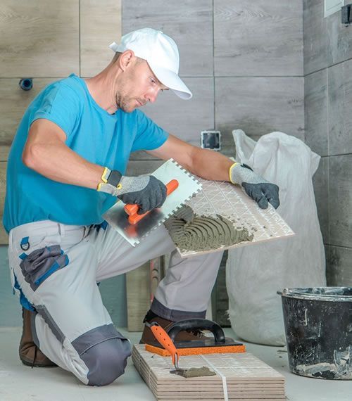 a man is kneeling and applying a tile with a trowel. Bathroom Gut and Remodel Cost in 2024
