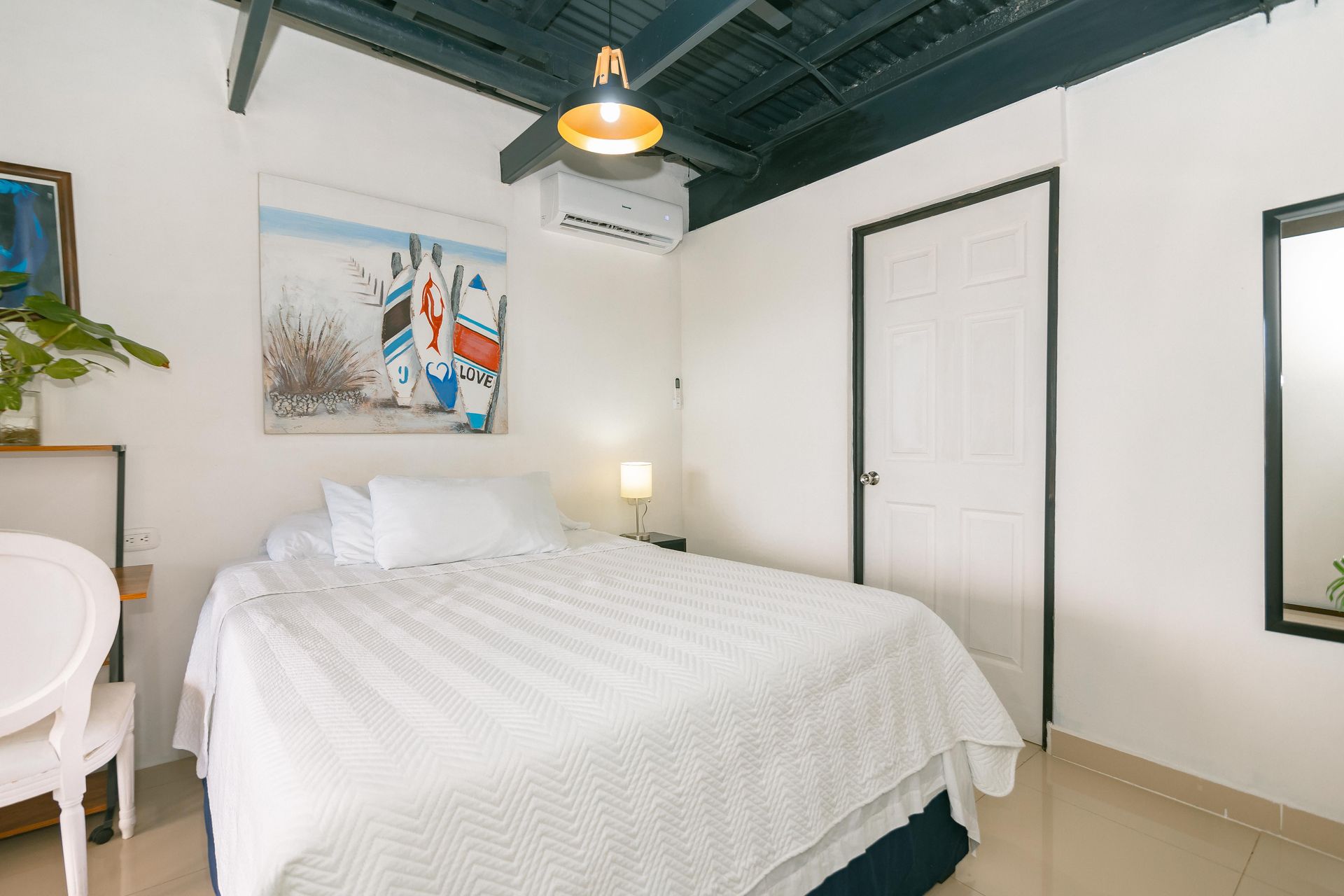 Un dormitorio con una cama, una silla, un espejo y un cuadro en la pared.