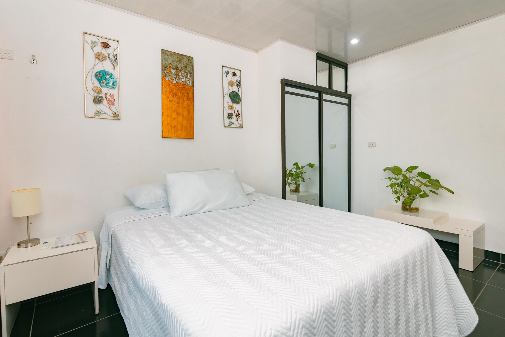 Un dormitorio con cama, mesita de noche, lámpara y cuadros en la pared.