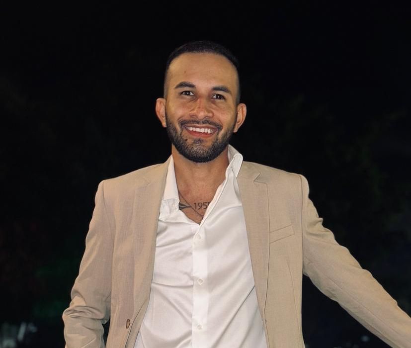 Un hombre con barba lleva una chaqueta color canela y una camisa blanca.