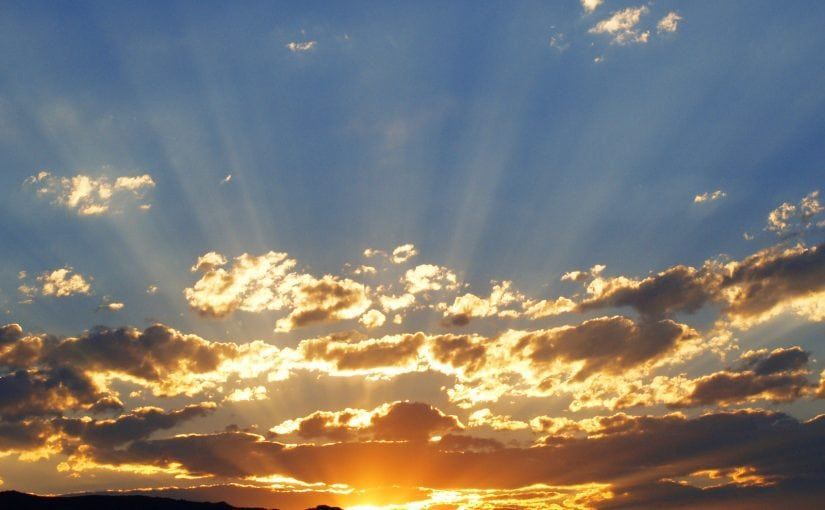 Sunset sky with sunbeams breaking through clouds; orange and yellow hues.