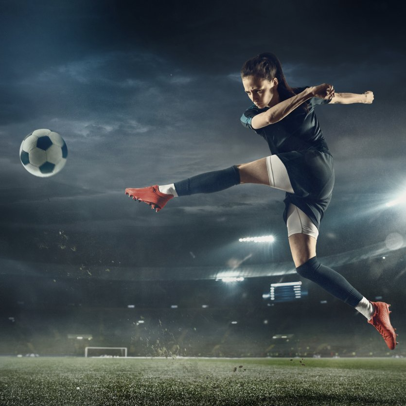 A female soccer player is kicking a soccer ball on a field.