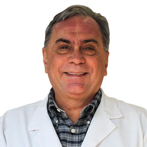 A man wearing a white lab coat and a plaid shirt is smiling.