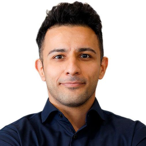 A man in a blue shirt is smiling with his arms crossed.