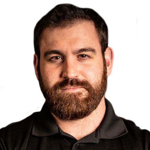 A man with a beard is wearing a black shirt and looking at the camera.