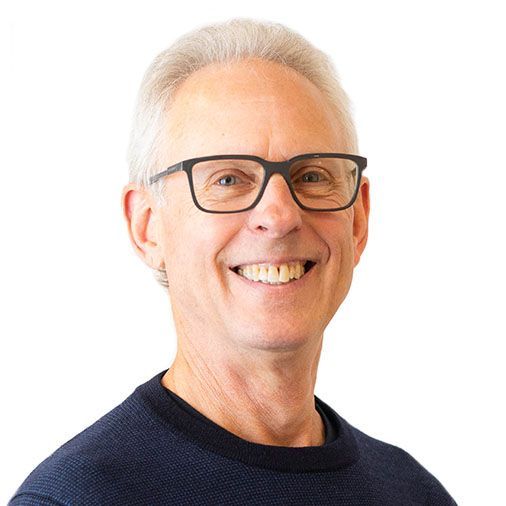 A man wearing glasses and a blue sweater is smiling for the camera.