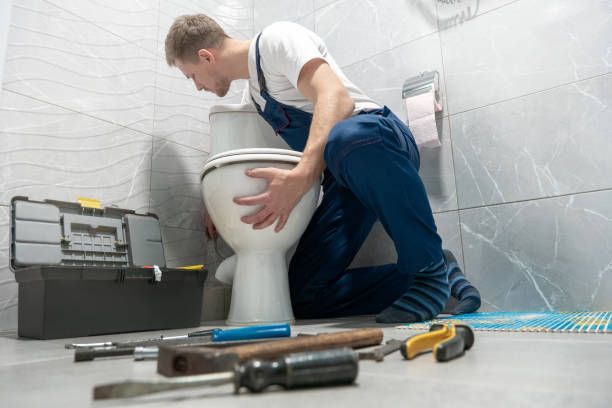 A plumber is kneeling down to fix a toilet in a bathroom.