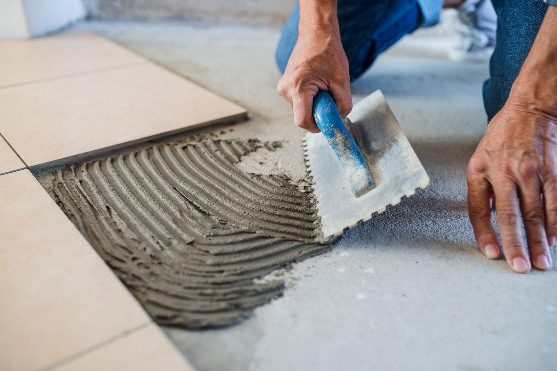 A man is laying tiles on the floor with a trowel.
