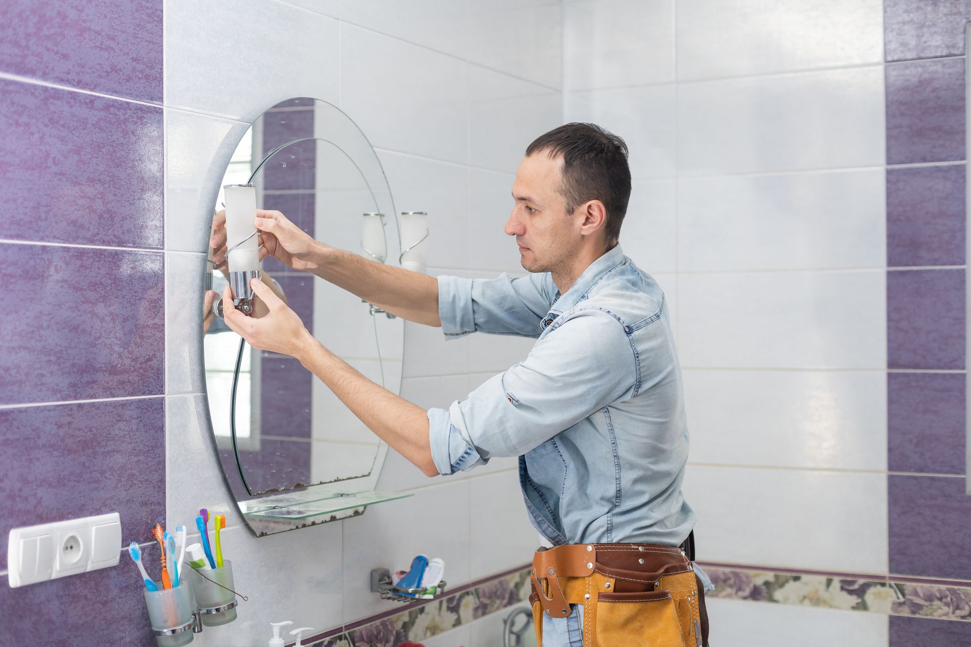 A man is fixing a mirror in a bathroom.