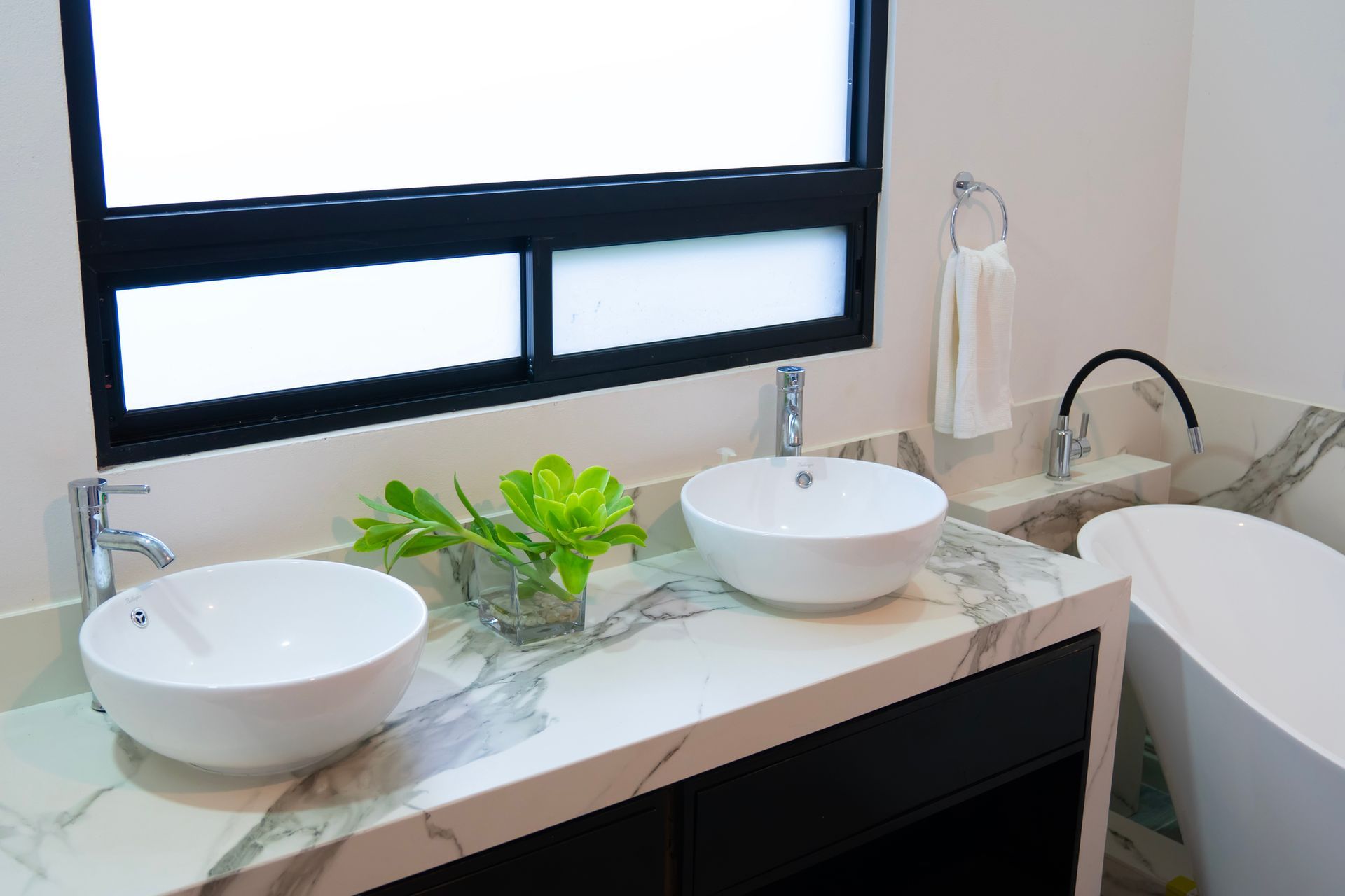 A bathroom with two sinks , a tub and a window.