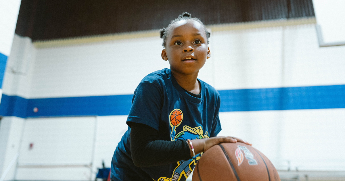 Young person with basketball in gym, looking up.