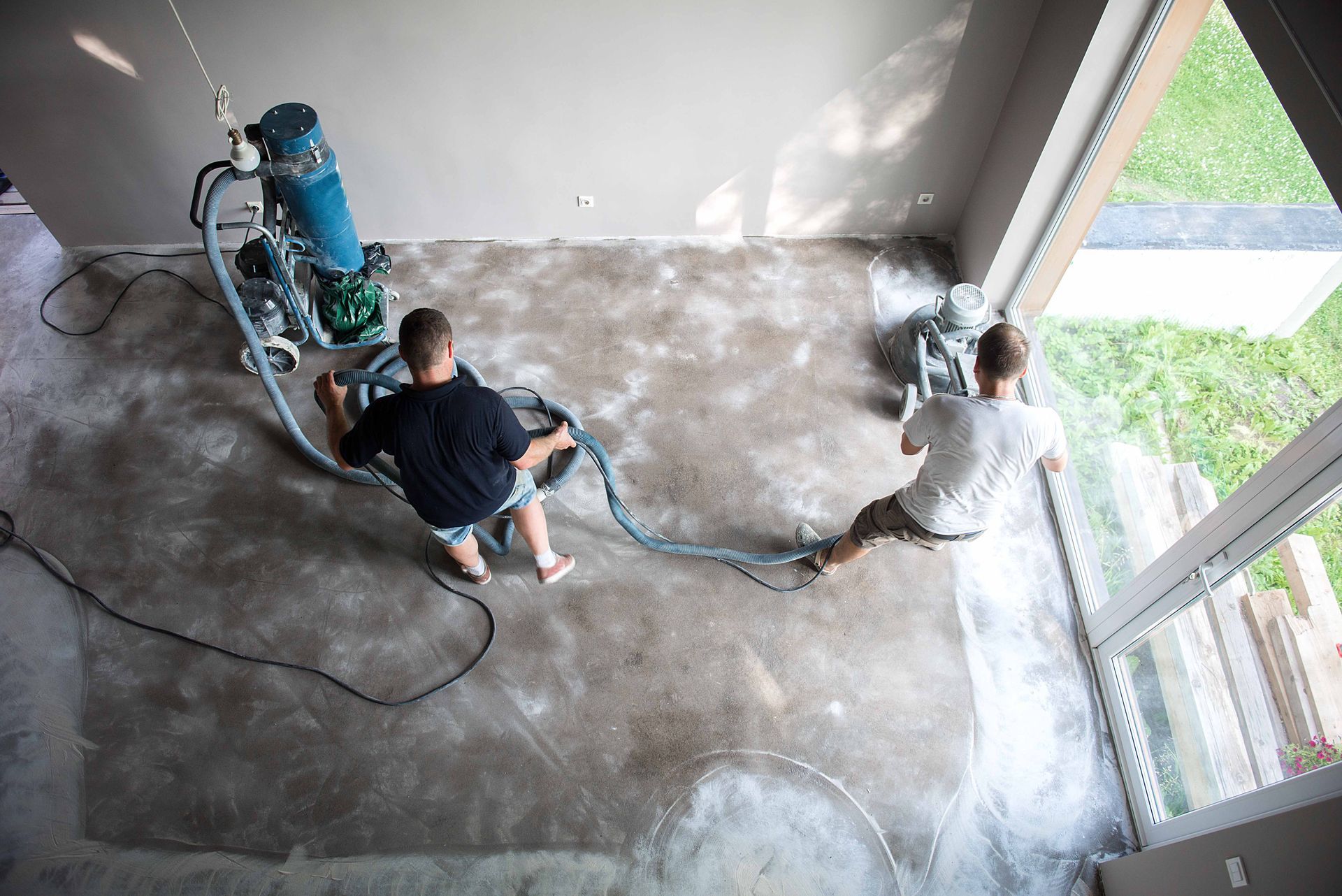 two men are working on a concrete floor in a room with concrete grinder .