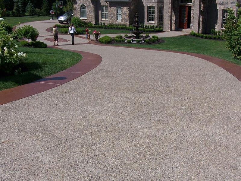 A driveway leading to a large house with a fountain in the middle