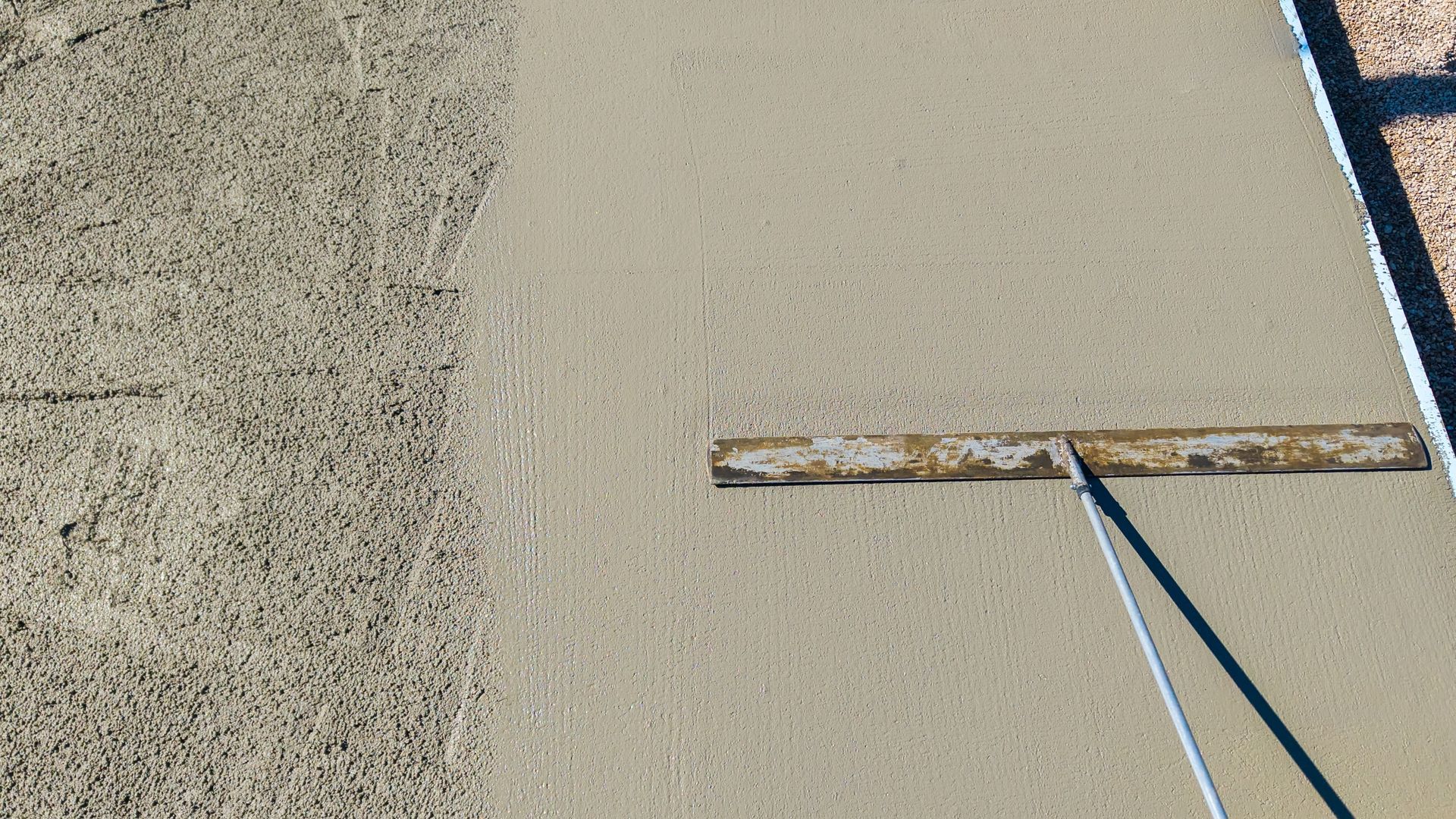 A person is spreading concrete on the ground with a trowel.