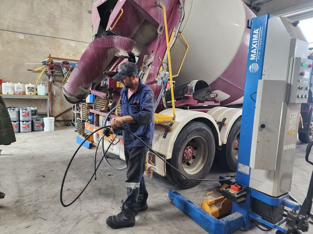 A man is standing next to a concrete mixer truck in a garage.