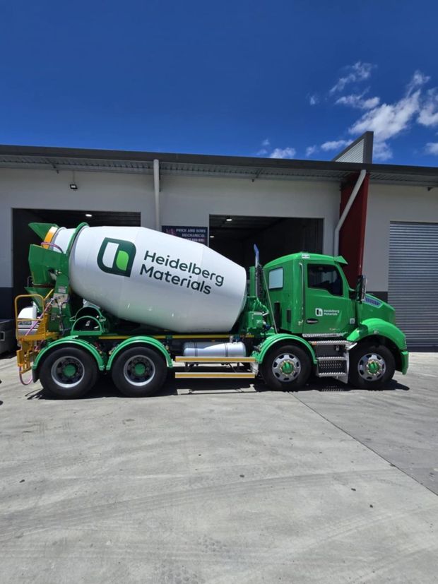 A green and white concrete mixer truck is parked in front of a building.