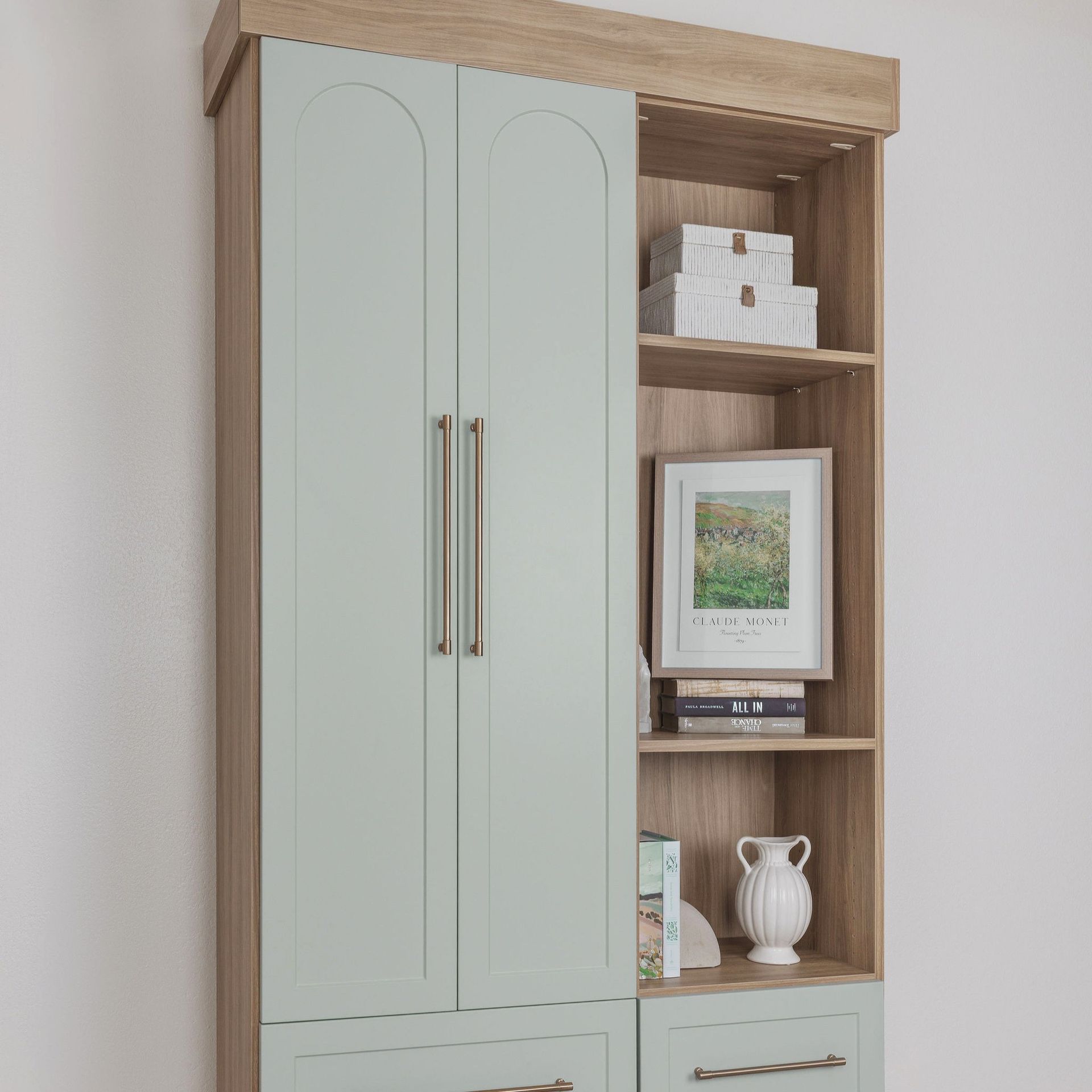 Light wood cabinet with pale green doors and open shelves holding framed art and decor