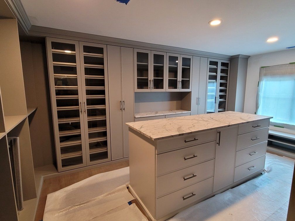 A walk in closet with lots of cabinets and drawers and a large island in the middle.
