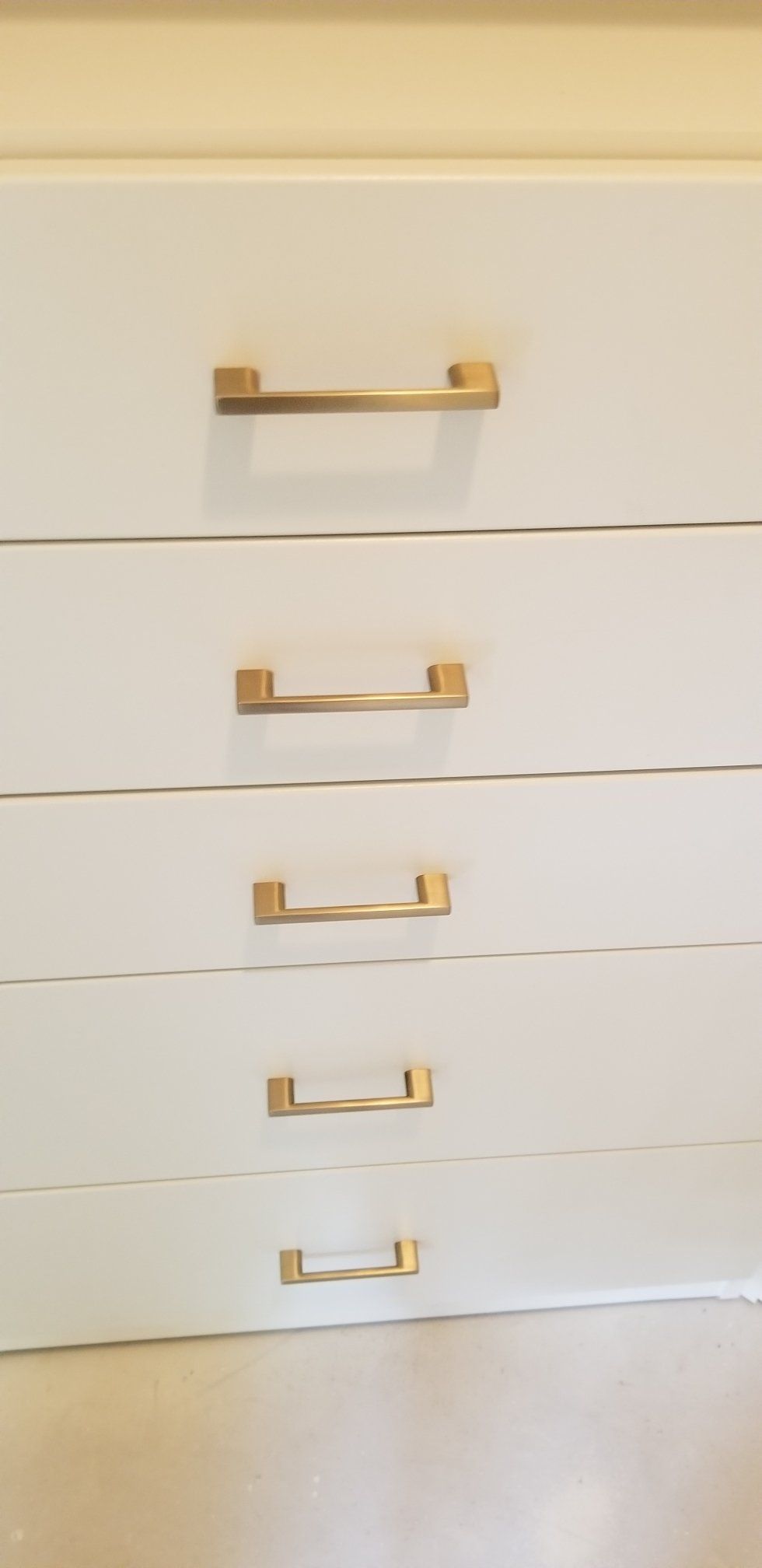 A close up of a white dresser with gold handles.