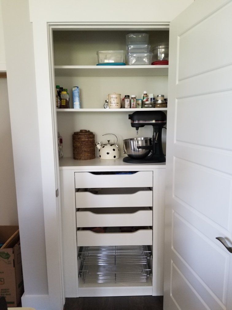 A pantry with drawers and shelves in a kitchen with a door open.