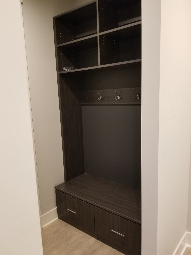 A closet with a bench , shelves , hooks and drawers.