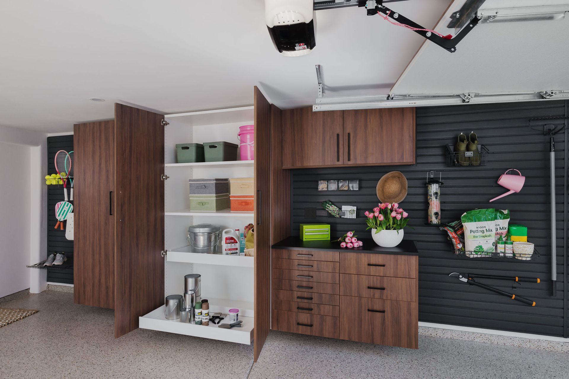 Garage with open shelving, cabinets, and a black slat wall displaying plants and storage items.