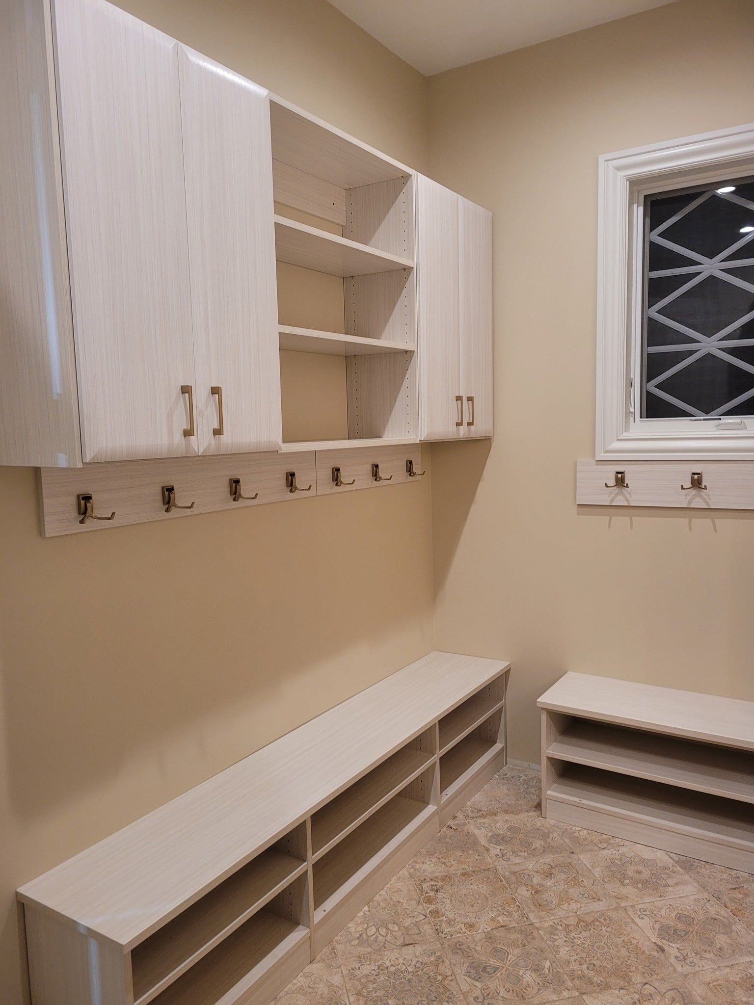 A room with a bench , shelves , hooks and a window.