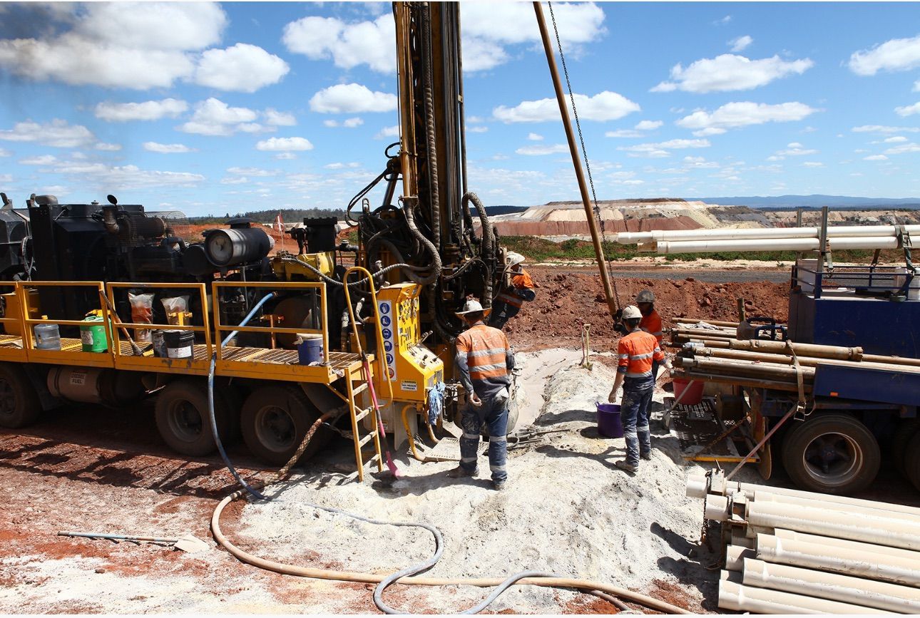 Drilling rig in a red dirt environment with workers in orange safety vests and hard hats.
