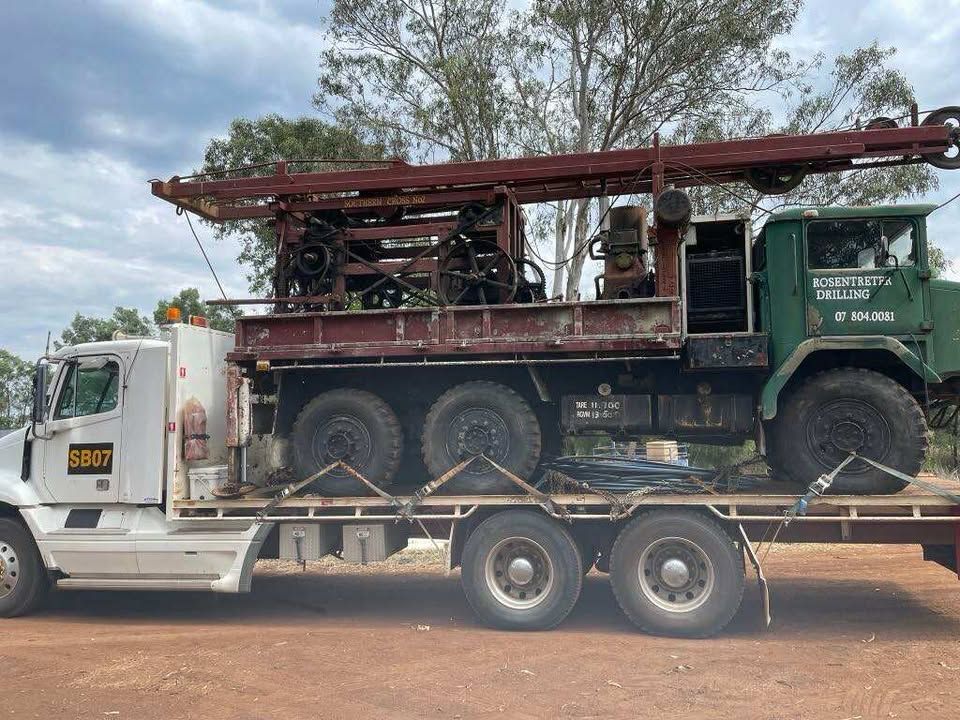 Well drilling rig loaded on a flatbed truck, outdoors, bright daylight.