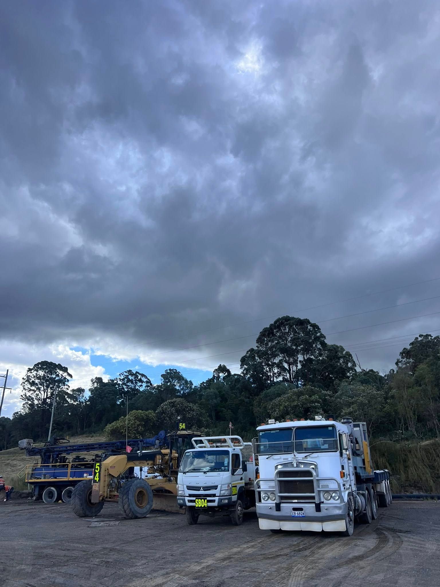 Three utility trucks parked under a cloudy sky, with trees in the background.