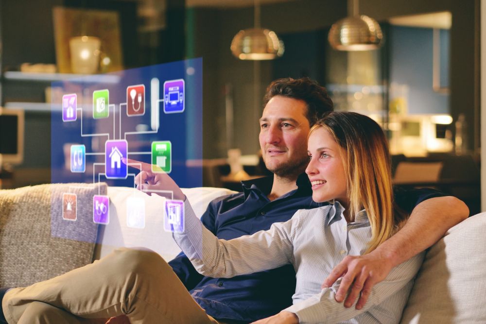 A Couple Sitting on The Sofa Controls All The Functions of The House — Wholesale Window Coverings in Lake Macquarie, NSW